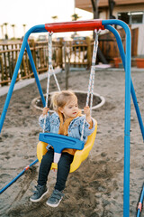 Fototapeta na wymiar Little girl swings on a colorful plastic swing and looks away