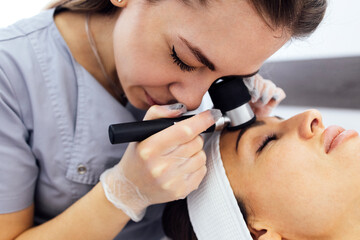 Doctor dermatologist examines skin of client face of beauty salon with a dermatological lens