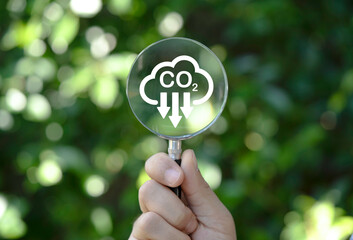 Hand holding magnifier glass with reduction carbon emission icon for zero carbon emission , CO2...