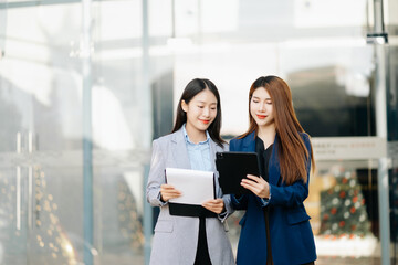 Businesswoman and woman going in city center in smart casual business style, talking, working together, stylish freelance people, holding tablet