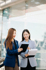 Fototapeta premium Businesswoman and woman going in city center in smart casual business style, talking, working together, stylish freelance people, holding tablet