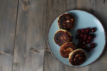 Burnt food cheesecakes on a blue plate on a gray background with space for text. Cottage cheese pancakes with cherry berries Copy Space