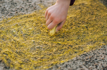 A diligent Ukrainian girl, a child draws a drawing of the sun with yellow chalk in her hand on the asphalt on the street in a park in Ukraine. Close-up photography, design, childhood concept.