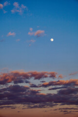 A clear evening sky with the moon visible, surrounded by dark clouds.