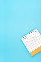 Desk calendar for February 2024 and white paper clip on a light blue.
