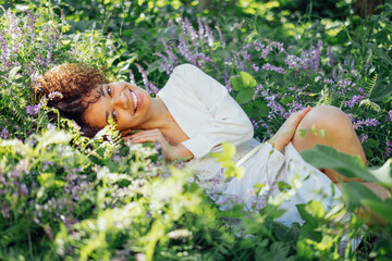 Attractive mixed race girl in white elegant chiffon dress sits among blooming purple flower