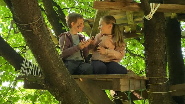 The joy of childhood by spending leisure time in a summer treehouse outdoors. Carefree elementary age kids playing at a play area on a tree. Playful atmosphere cherished memories in the great outdoors