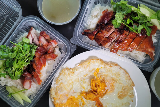 A take away plastic box of Chinese style roasted duck rice with fried egg serving on a plate, top view image.