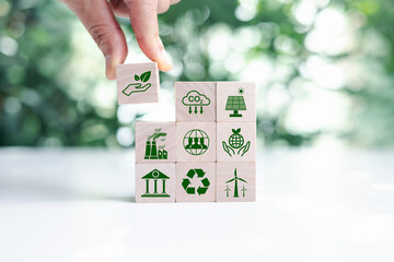 Hand put wooden cubes with green net zero icon and green icon on bokeh nature. Net zero and carbon neutral concept. Net zero greenhouse gas emissions target. Climate neutral long term strategy.