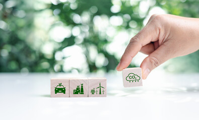 Hand put wooden cubes with green net zero icon and green icon on bokeh nature. Net zero and carbon...