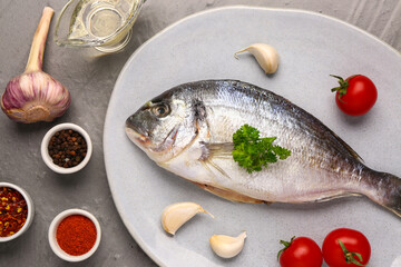 Plate of raw dorado fish with tomatoes and spices on grey background