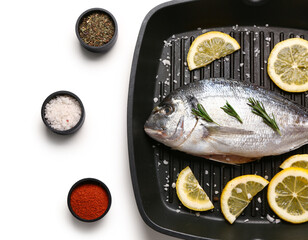 Grill pan of raw dorado fish with lemon and spices and on white background