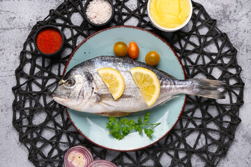 Plate of raw dorado fish with lemon and tomatoes on light background