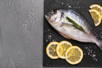 Slate board of raw dorado fish with lemon on grey background