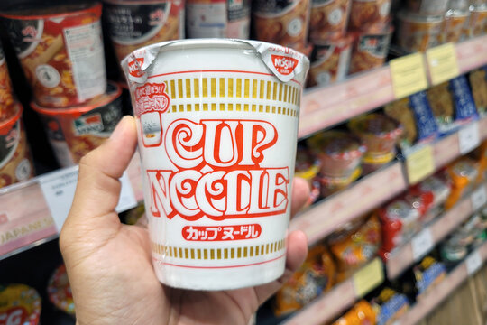 PENANG, MALAYSIA - 15 Dec 2023: Adult hand holding a Nissin brand Cup noodle. Instant noodles were invented in 1958 by Momofuku Ando, the Taiwanese-born founder of the Japanese food company Nissin.
