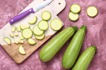 Fresh green zucchini and board with slices on purple background