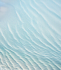 abstract white sand beach with transparent water wave from above, calm rippled water surface background concept with space for text or product presentation