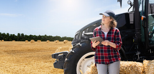 Woman farmer with a digital tablet next to agricultural tractor