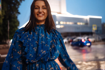 Beautiful brunette girl in blue dress laughs and dances in pouring rain in evening