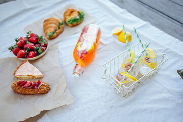 Bottle of strawberry and lemon smoothie, soda glasses with straws, herb croissants, sweet cakes and fresh strawberries