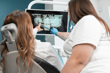 The dentist shows the patient a panoramic X-ray on the monitor, carefully explaining all the...