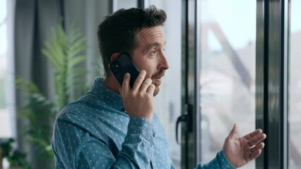 Video of businessman talking on mobile phone while standing next to the window in his office in a modern startup. - Powered by Adobe