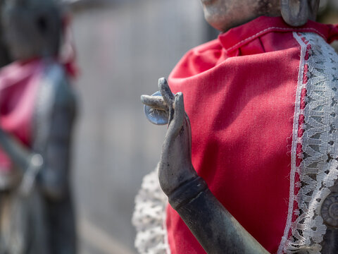 Japanese statue of bodhisattva Kannon in red bib with coin between fingers