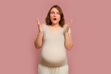A scared pregnant woman on a pink studio background. Pregnancy in a frightened woman with a belly