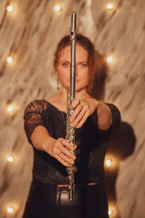 The flutist, a female musician, played her instrument under the illuminated concert lights at the musical entertainment.