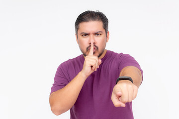 A stern man calling someone out to shut up and keep quiet. Hush gesture with finger. Wearing a purple shirt, isolated on a white background. - obrazy, fototapety, plakaty