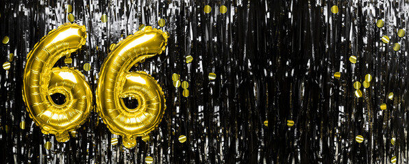 Gold foil balloon number number 66 on a background of black tinsel decoration. Birthday greeting...