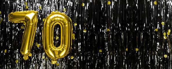Gold foil balloon number number 70 on a background of black tinsel decoration. Birthday greeting...