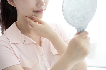 Young woman checking face with mirror