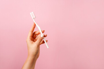 White Toothbrush in woman's hand on pink background with copy space