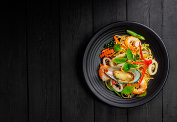 Seafood drunken spaghetti with shrimp squid clams chili, and basil. Thai food. Healthy Asian in a plate on a black background table. Top view.