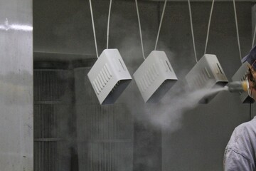 Powder coating of metal parts. Woman in protective suit sprays paint from gun on metal products. Painting technician applying paint to car part with spray gun. Auto repair in garage car body shop