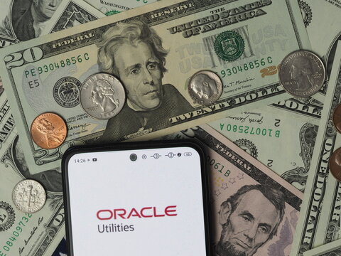 In this photo illustration, a Oracle Utilities  logo seen displayed on a smartphone with United States Dollar notes and coins in the background.