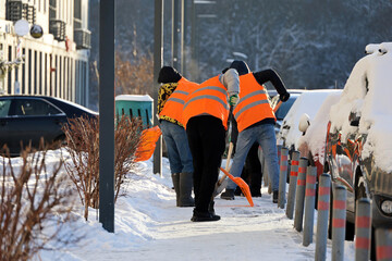 Workers with shovels cleaning sidewalk, snow and melting ice removal in winter city