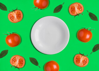 Empty white plate for text and red tomato on the green background. Copy space. Top view.