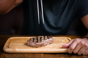 Entrecote steak on wooden board about to be stabbed by meat serving fork in restaurant