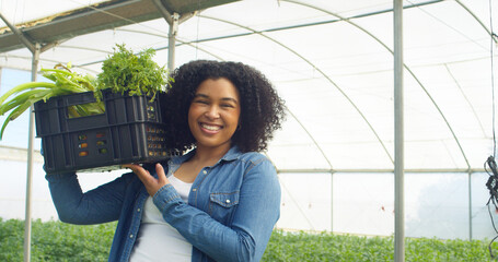 Portrait of Black woman farmer smiling and holding crate of vegetables on farm