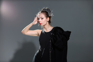 Studio portrait of beautiful young brunette woman in black dress with a crown on her head