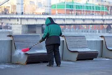 Snow removal, municipal worker with a broom clears snow on winter street. Man in uniform sweeps...