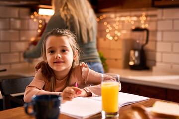 In the kitchen, a little preschooler enjoys breakfast and lets creativity flow, coloring with joy.