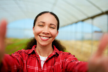 Multi-ethnic female farmer taking selfie with greenhouse in background