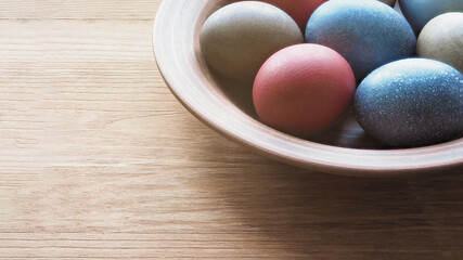 Clay plate with colored eggs for Easter on wooden surface, close-up, copy space.