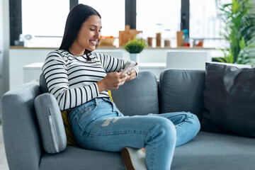 Pretty young smiling woman using mobile phone sitting on a couch at home.