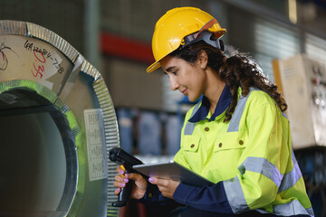 Smiling woman supervisor in a factory or warehouse, wearing a hardhat and ensuring safety on the industrial site, perform quality checks inside a metal sheet factory.