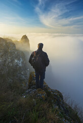 Autumn morning. Traveler on the top of rock above river valley with thick fog. Nature of Ukraine