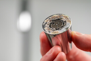 A plumber is holding a chrome faucet aerator with lime scale in kitchen